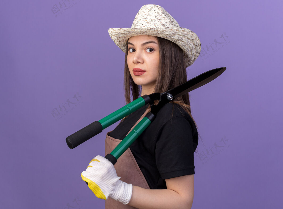 女自信漂亮的白人女园丁戴着园艺帽子和手套站在一边 手里拿着紫色的园艺剪刀站立漂亮侧身