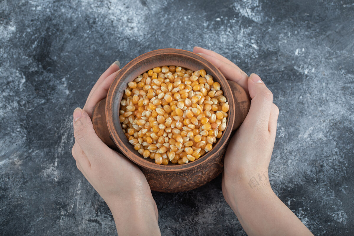玉米手里拿着一个盛满未煮过的爆米花籽的古老碗有机食物顶视图