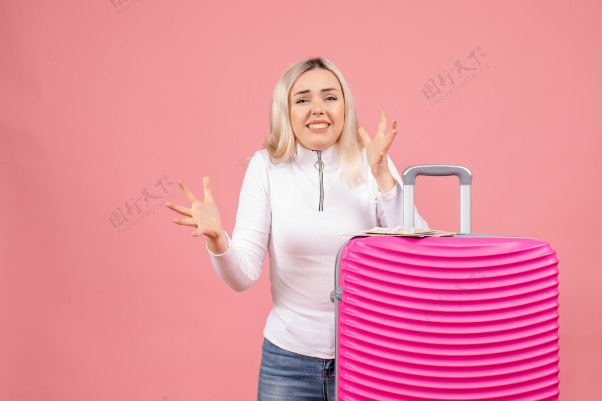 漂亮正面图：站在粉色手提箱后面的激动的年轻女士可爱手提箱微笑