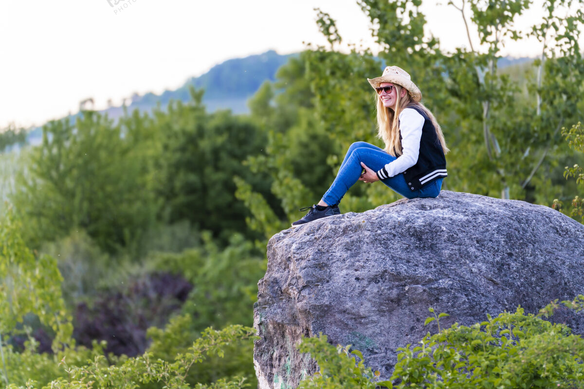 美丽浅焦拍摄的欧洲女性与牛仔帽坐在岩石上的性质牛仔年轻欧洲