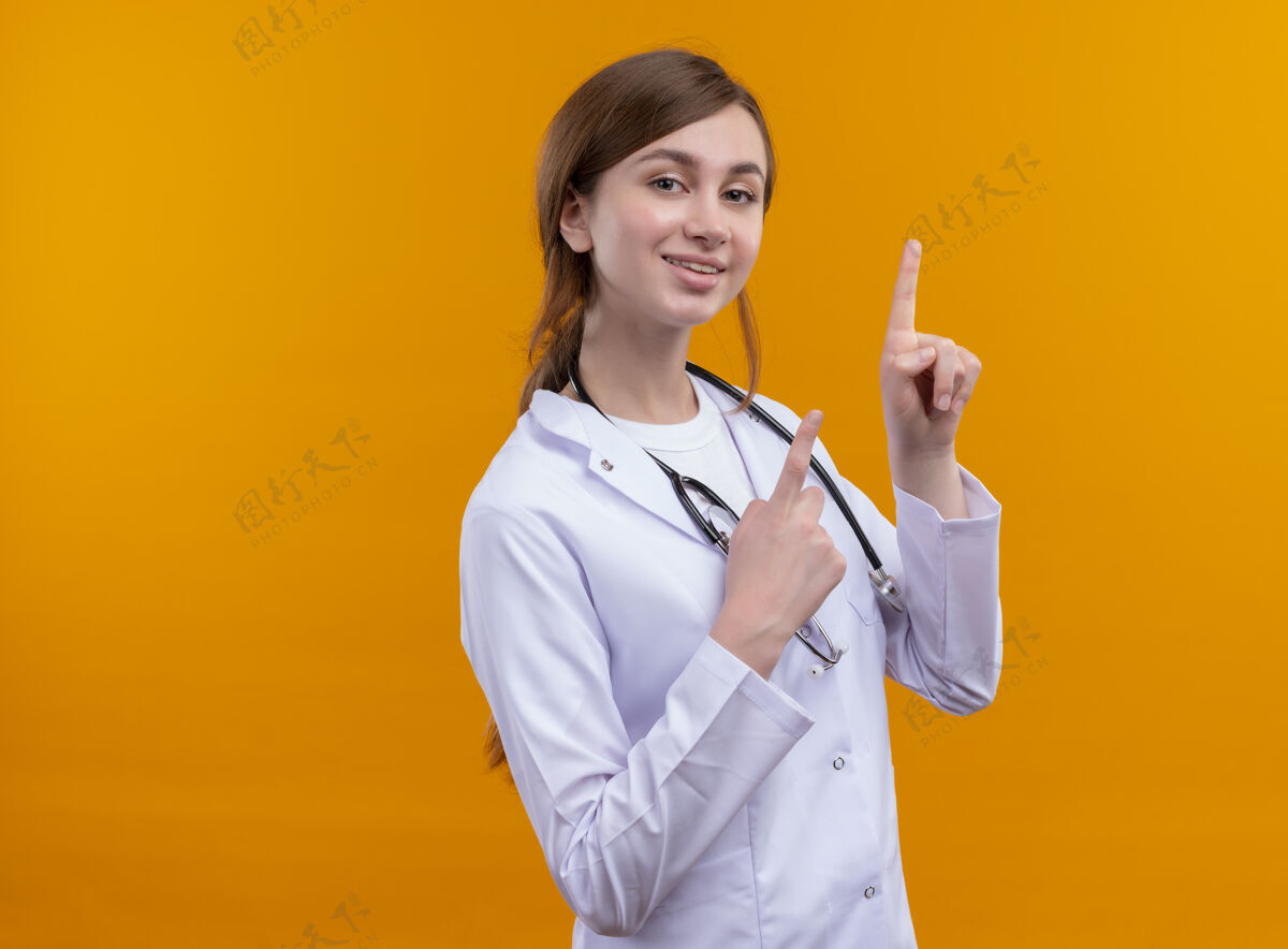复制令人印象深刻的年轻女医生穿着医用长袍和听诊器指着孤立的橙色空间与复制空间指向年轻穿着