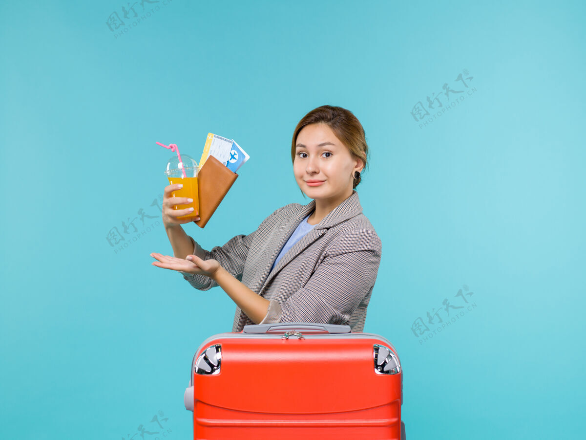 微笑正面图：度假中的女性手持新鲜饮料和浅蓝色背景的机票出海度假女人旅行桶