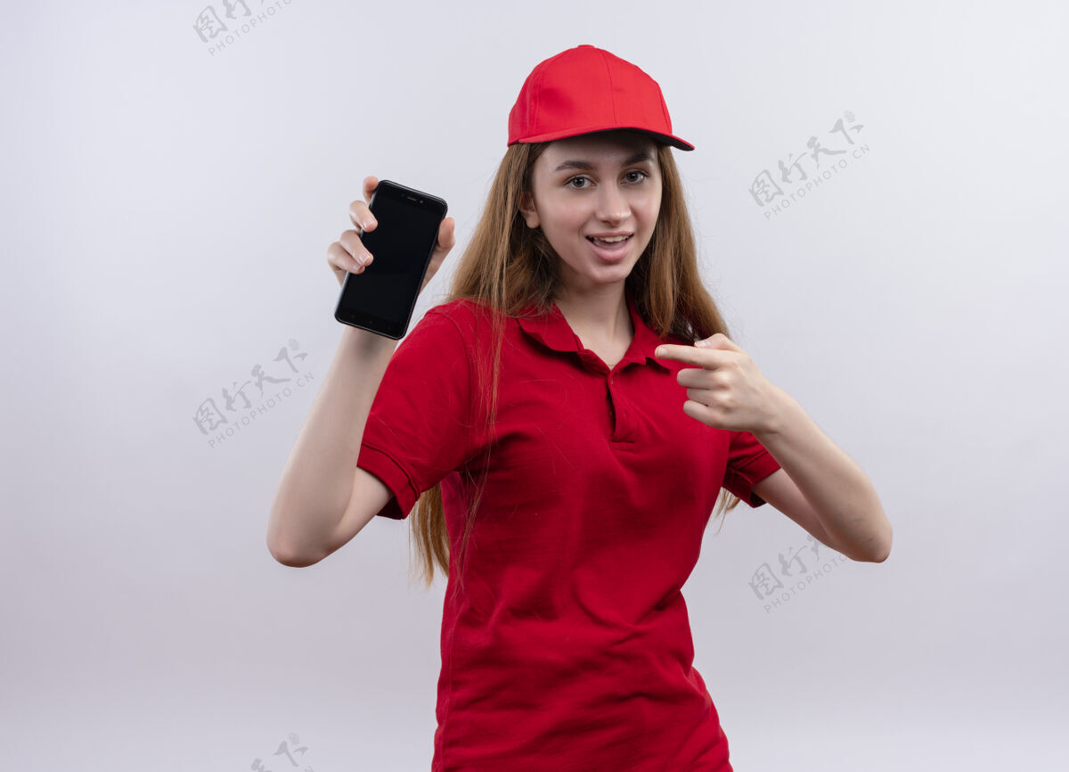 送货快乐的年轻送货女孩穿着红色制服 拿着手机指着与世隔绝的白色空间年轻红色快乐