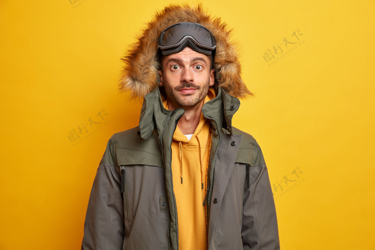 严肃严肃的未刮胡子的男子游客冬天在山上休息 喜欢穿着暖和的夹克和皮帽滑雪看起来很自信季节时尚站