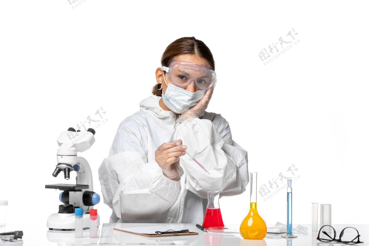 工作服正面图：穿着防护服 戴着口罩的女医生正在用白色办公桌上的病毒冠状病毒解决方案工作正面男人视图