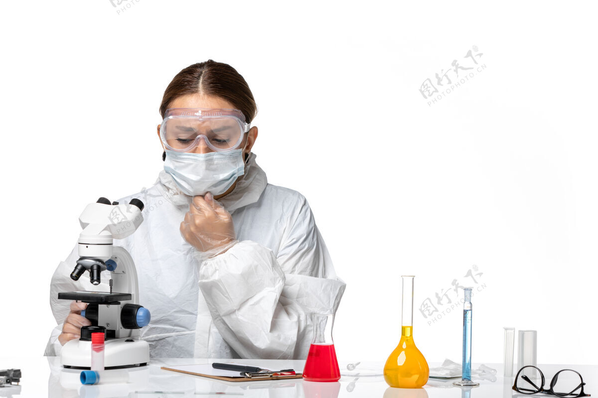防护罩前视图穿着防护服 戴着口罩的女医生用显微镜观察了一种白色背景的医学冠状病毒-健康大流行病毒健康正面病毒