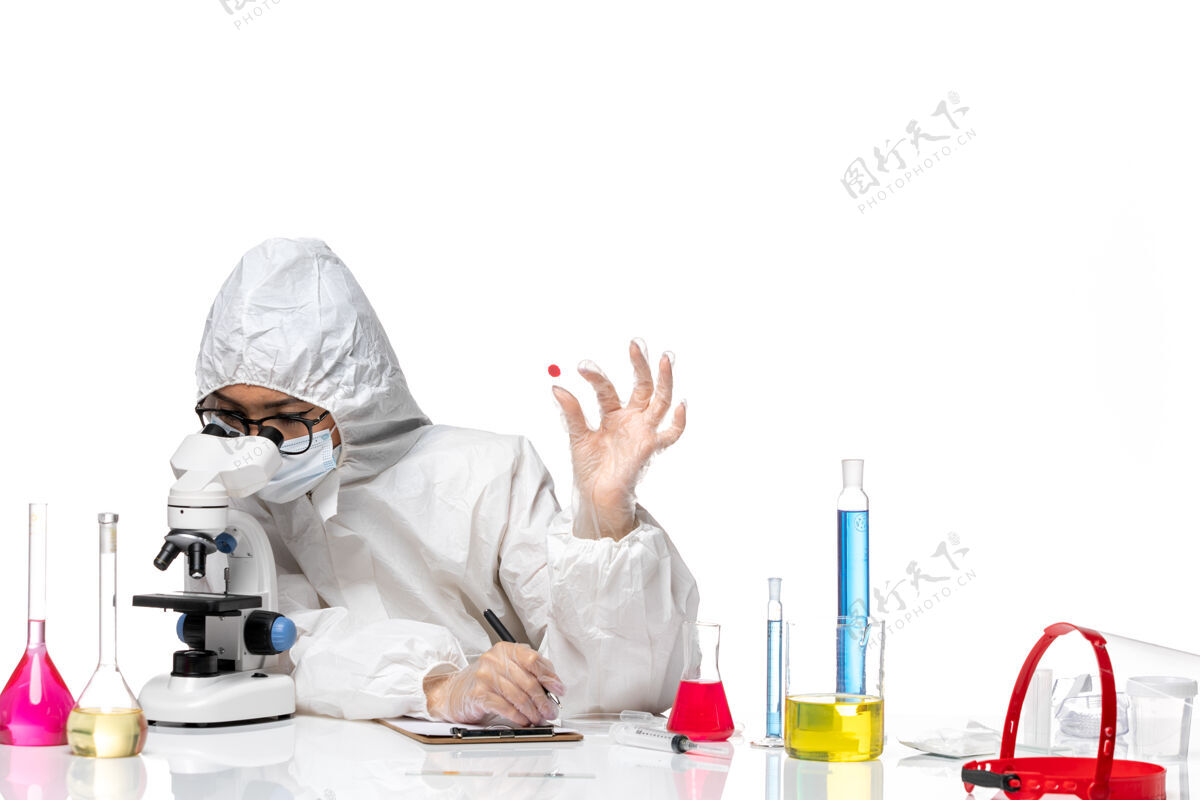工作正面图穿着特殊防护服的女化学家正在检查白桌子上的样本病毒化学疫苗大流行健康医生样本健康