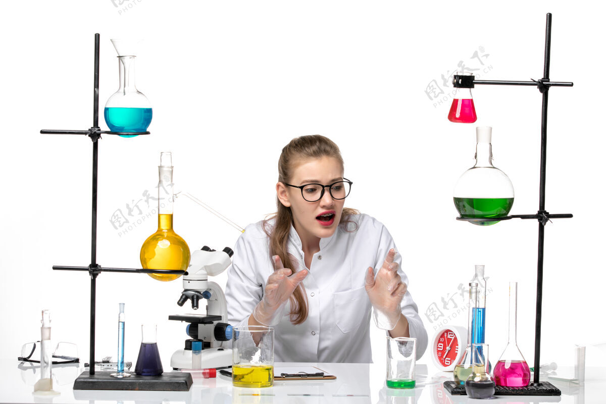 前面前视图穿着医疗服的女化学家坐在浅白的背景上 解决了化学大流行性冠状病毒烧杯医学医学