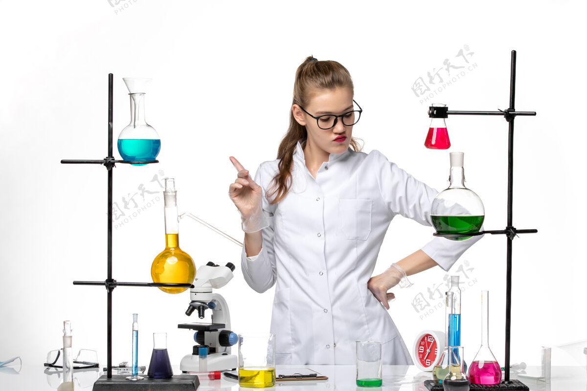 女化学家正面图：身着医疗服的女化学家在工作过程中用白色办公桌上的溶液化学大流行病毒人工作药