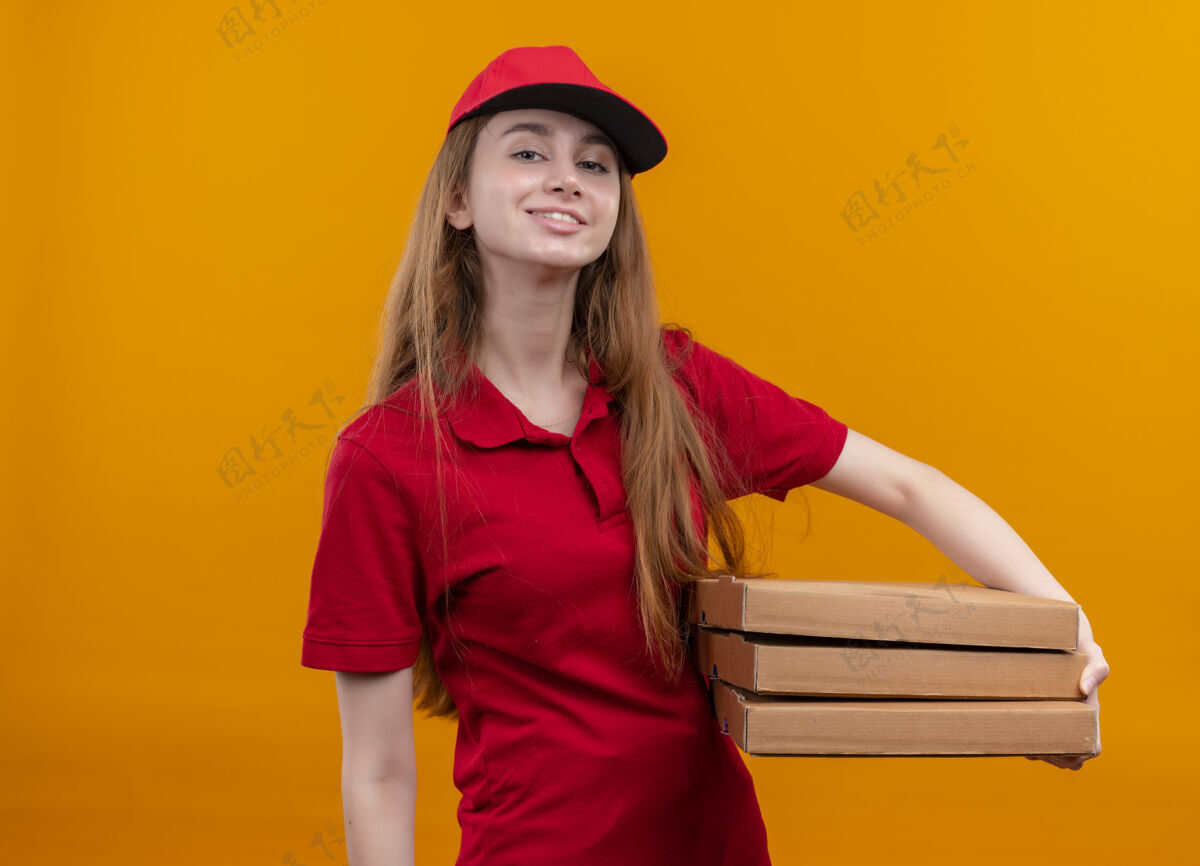 女孩自信的年轻送货女孩穿着红色制服拿着包裹在孤立的橙色空间盒持有交付
