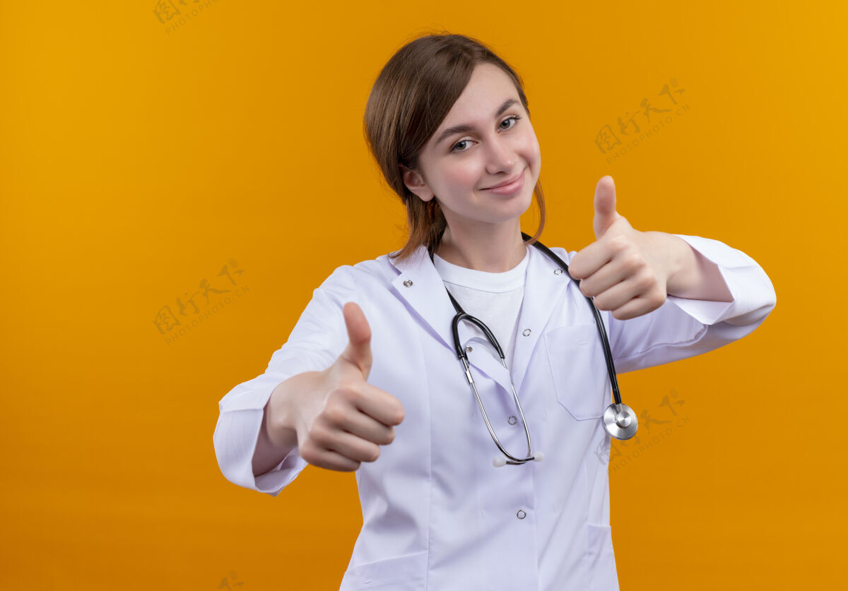 长袍自信的年轻女医生穿着医用长袍和听诊器 在孤立的橙色空间和复印空间上竖起大拇指橙色年轻医疗