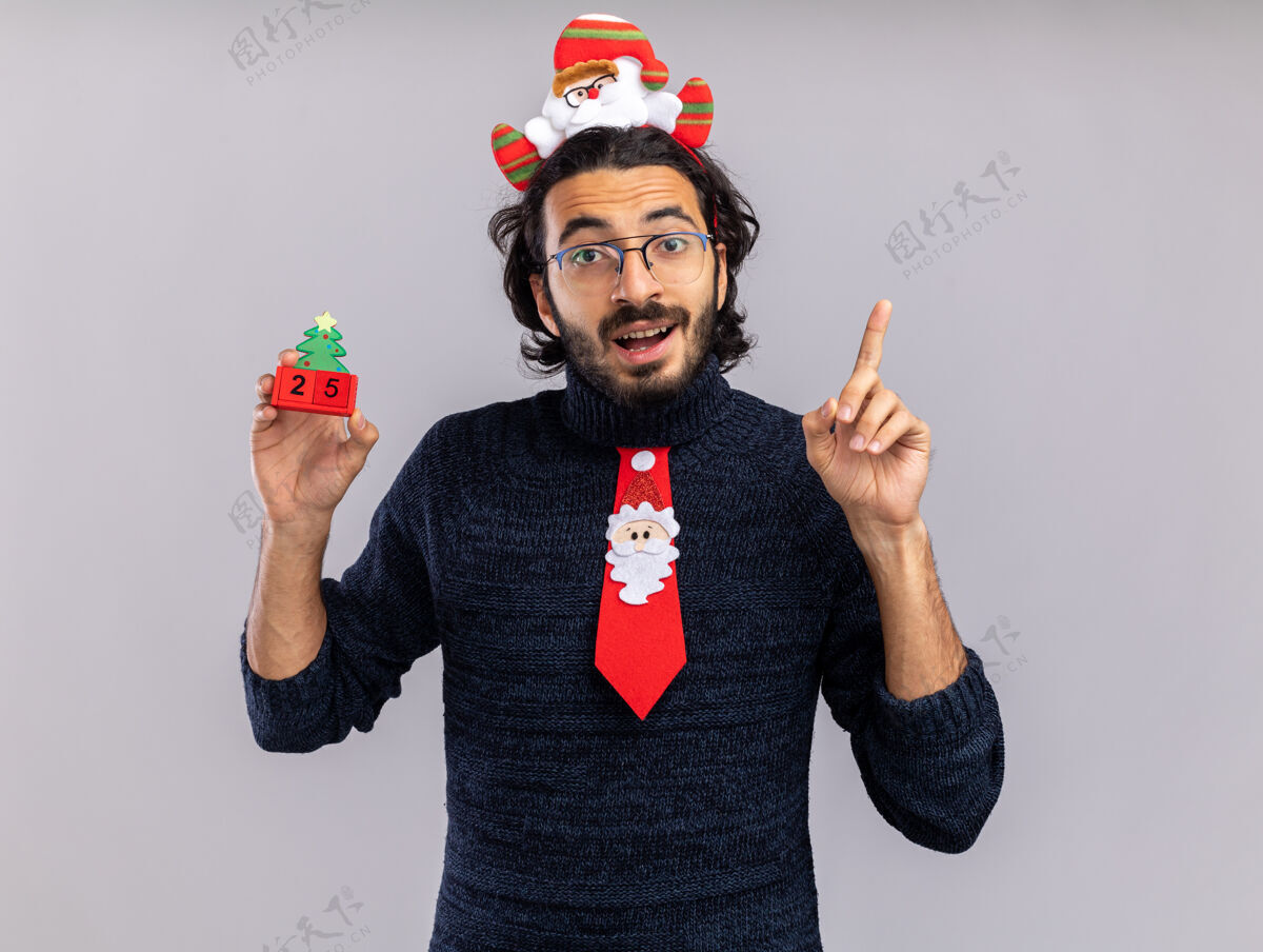 圣诞节印象深刻的年轻帅哥戴着圣诞领带 戴着发箍 拿着圣诞玩具点在白色背景上孤立起来圣诞快乐白色家伙