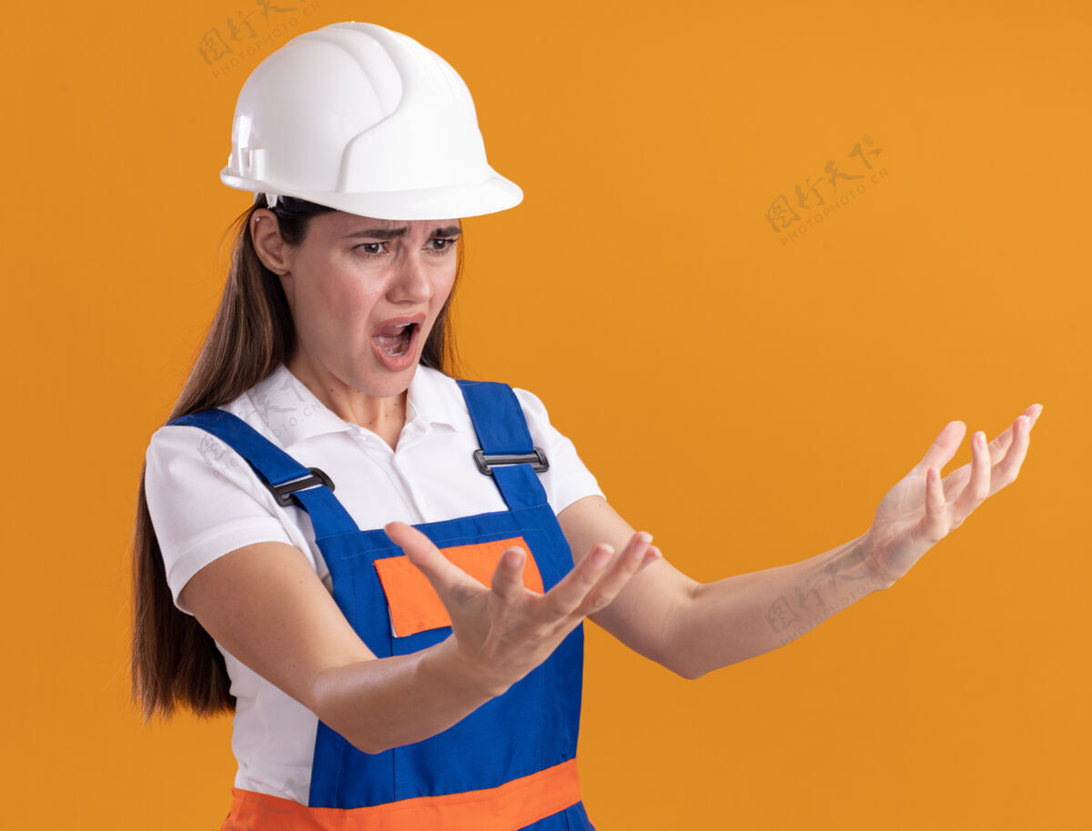 女人愤怒地看着一旁穿着制服的年轻建设者女子在一旁伸出双手孤立在橘色的墙上制服抱着人