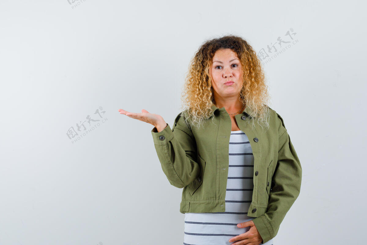 手掌美丽的金发女人的肖像摊开手掌在绿色夹克衫旁边 看着困惑的前视图问题表情肖像
