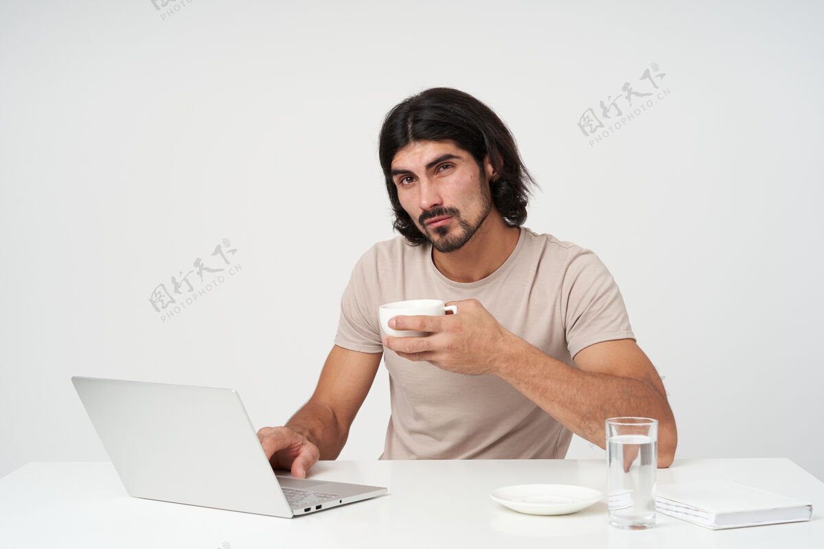 学生帅气的男性 英俊的商人 黑头发 黑胡子办公室概念坐在工作场所喝咖啡休息拿着杯子隔着白墙外表人脸