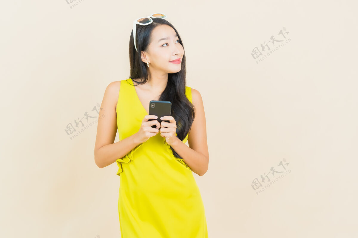 休闲美丽的亚洲年轻女子在彩色墙上用智能手机微笑应用程序电话漂亮