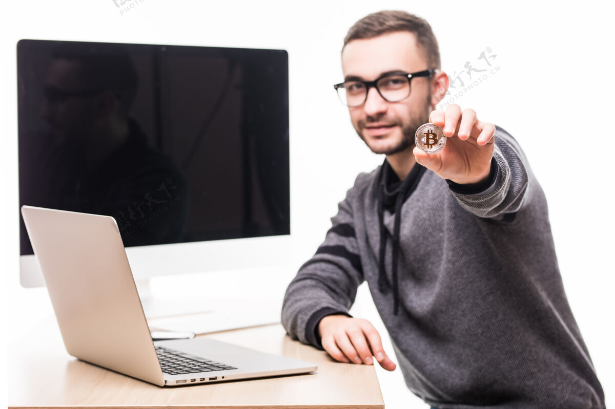 商业帅哥坐在办公室里 背着笔记本电脑和显示器屏幕 把比特币指向白色加密经济商业