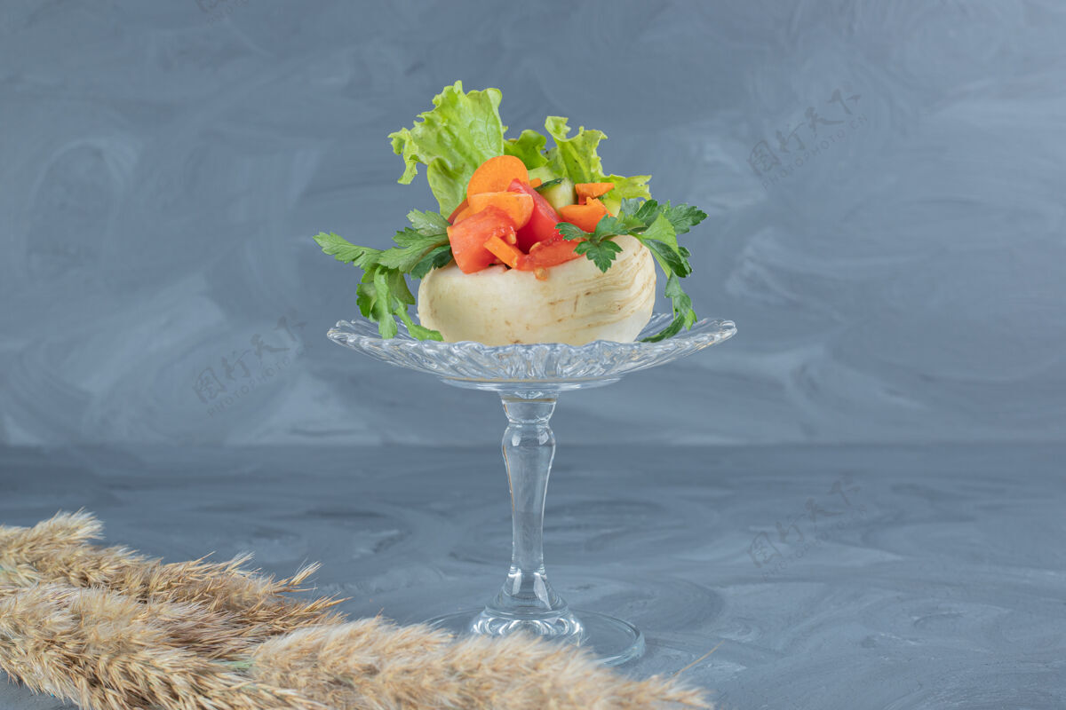胡萝卜切碎的蔬菜放在玻璃基座上的白萝卜上 大理石桌上放着针叶草茎美味欧芹黄瓜