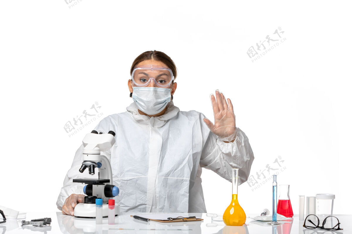 白人前视图女医生穿着特殊的西装 戴着口罩 用显微镜观察白色背景的冠状病毒大流行工作医生套装