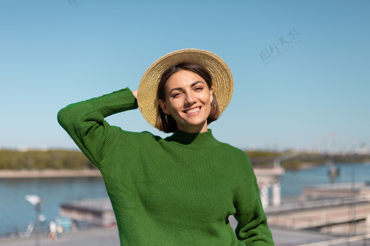 旅游穿着绿色休闲毛衣 戴着帽子的时尚女士在户外的桥上欣赏河景 享受夏日阳光明媚的日子欢乐蓝色旅游