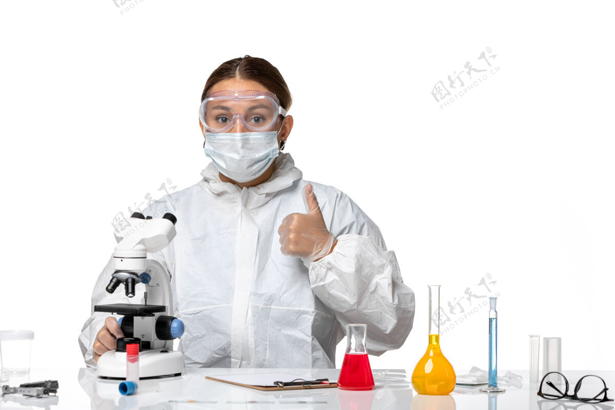 套装正面图女医生穿着防护服 戴着口罩 用显微镜对白色背景健康大流行的冠状病毒医疗实验室正面