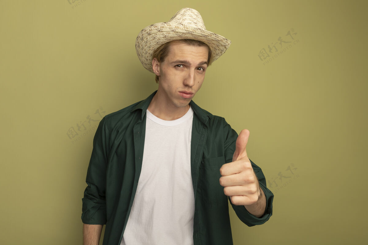 拇指年轻的金发小伙子穿着绿色t恤 戴着帽子 竖起大拇指秀年轻人