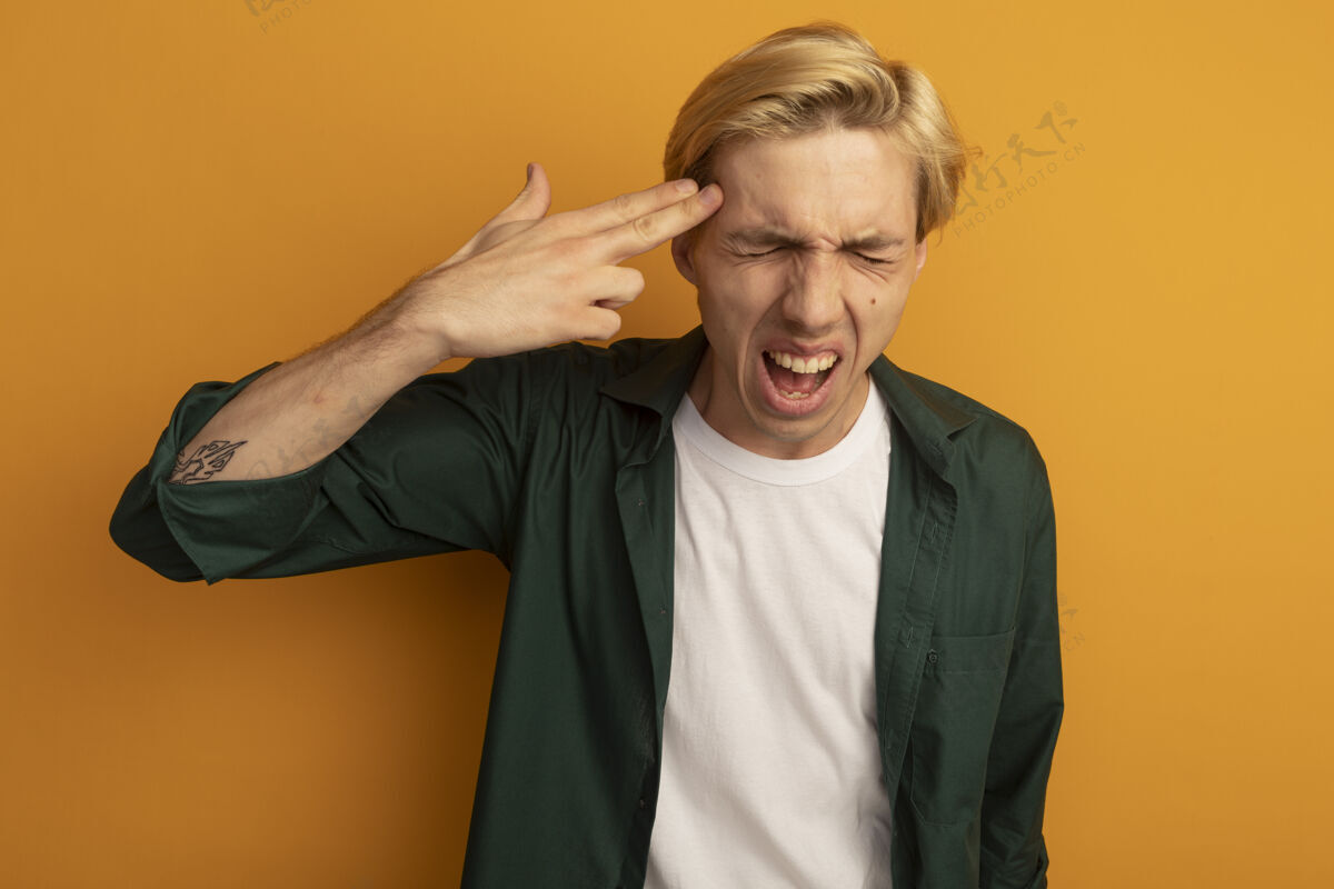 男人愤怒与闭上眼睛年轻的金发男子穿着绿色t恤显示与手枪自杀的手势黄色秀眼睛