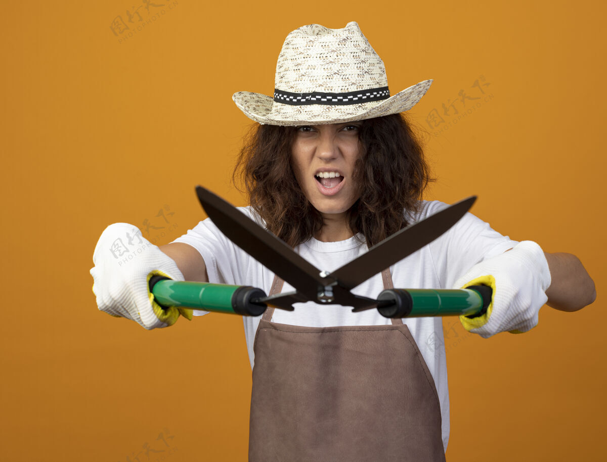 穿穿着制服的年轻女园丁兴奋地戴着园艺帽和手套 手里拿着剪刀女人制服手套