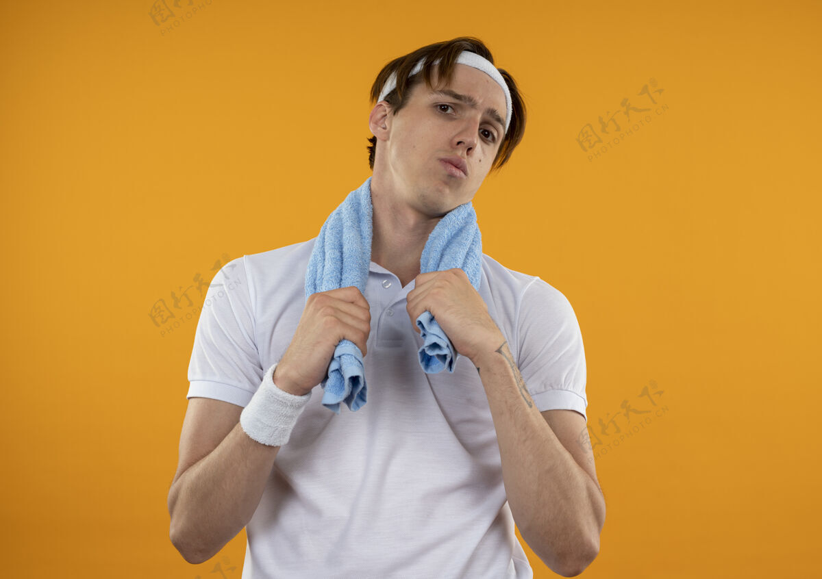 头带戴着头带和腕带 肩上挂着毛巾的年轻运动型男人被隔离在橙色的墙上肩膀穿不愉快