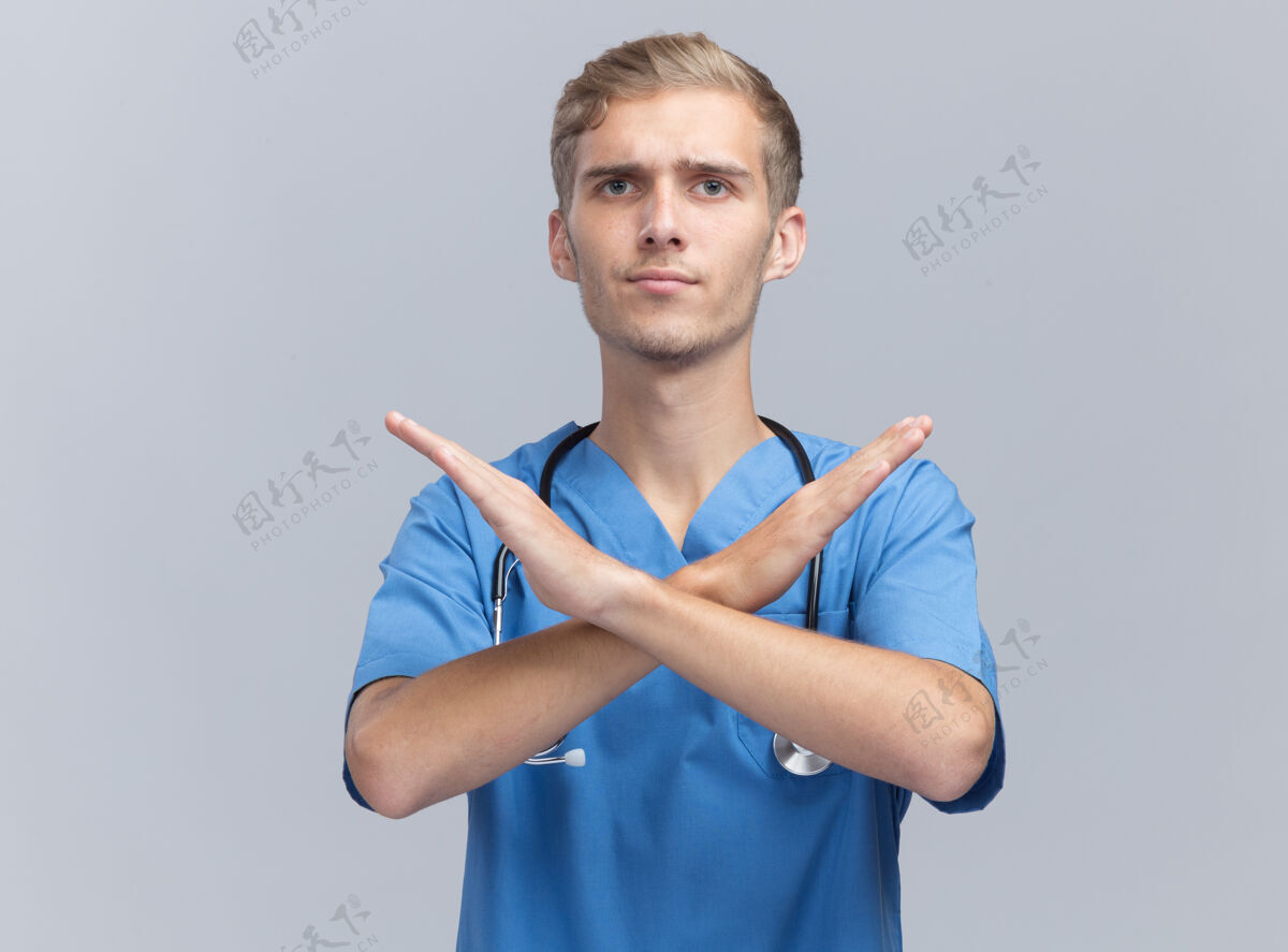 男性严格的年轻男医生穿着医生制服 听诊器显示没有孤立的姿态在白墙上听诊器制服年轻