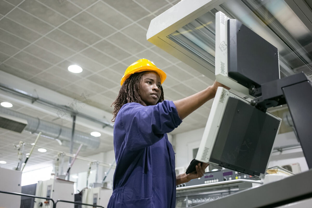 工作专注自信的工厂女工操作工业机器 触摸控制板 使用平板电脑年轻人制服女性