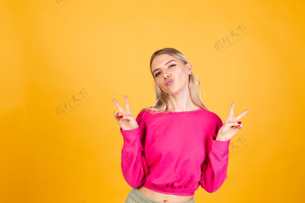 休闲黄色墙上穿粉红色上衣的漂亮欧洲女人成功享受手指