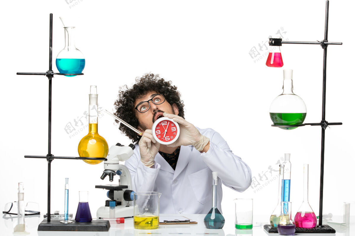 实验室正面图身穿医疗服的男科学家拿着浅白色桌子上的红色时钟专业科学桌子