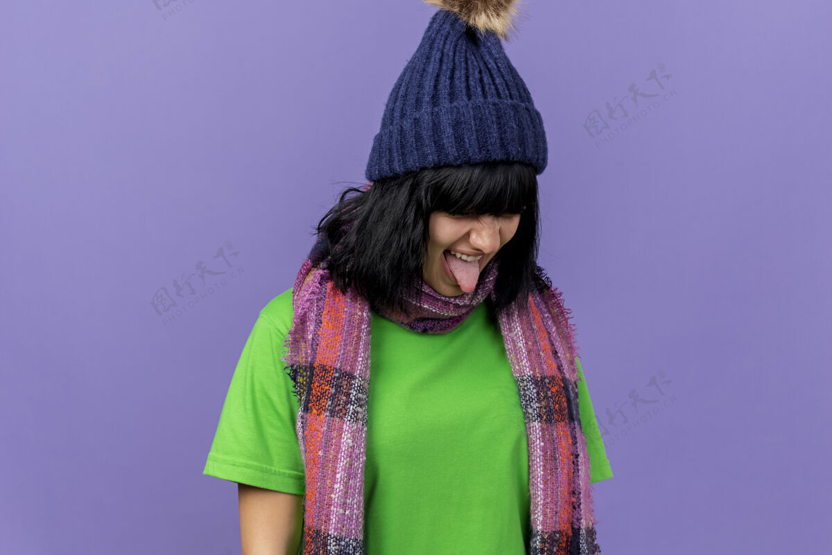 穿愁眉苦脸的年轻病妇戴着冬天的帽子和围巾把头转向一边 在紫色的墙壁上露出孤立的舌头 还有复制空间围巾侧线感情