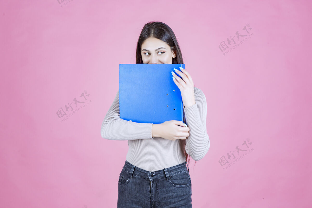 新的女孩拿着一个蓝色的项目文件夹 把她的脸藏在后面助理女人人