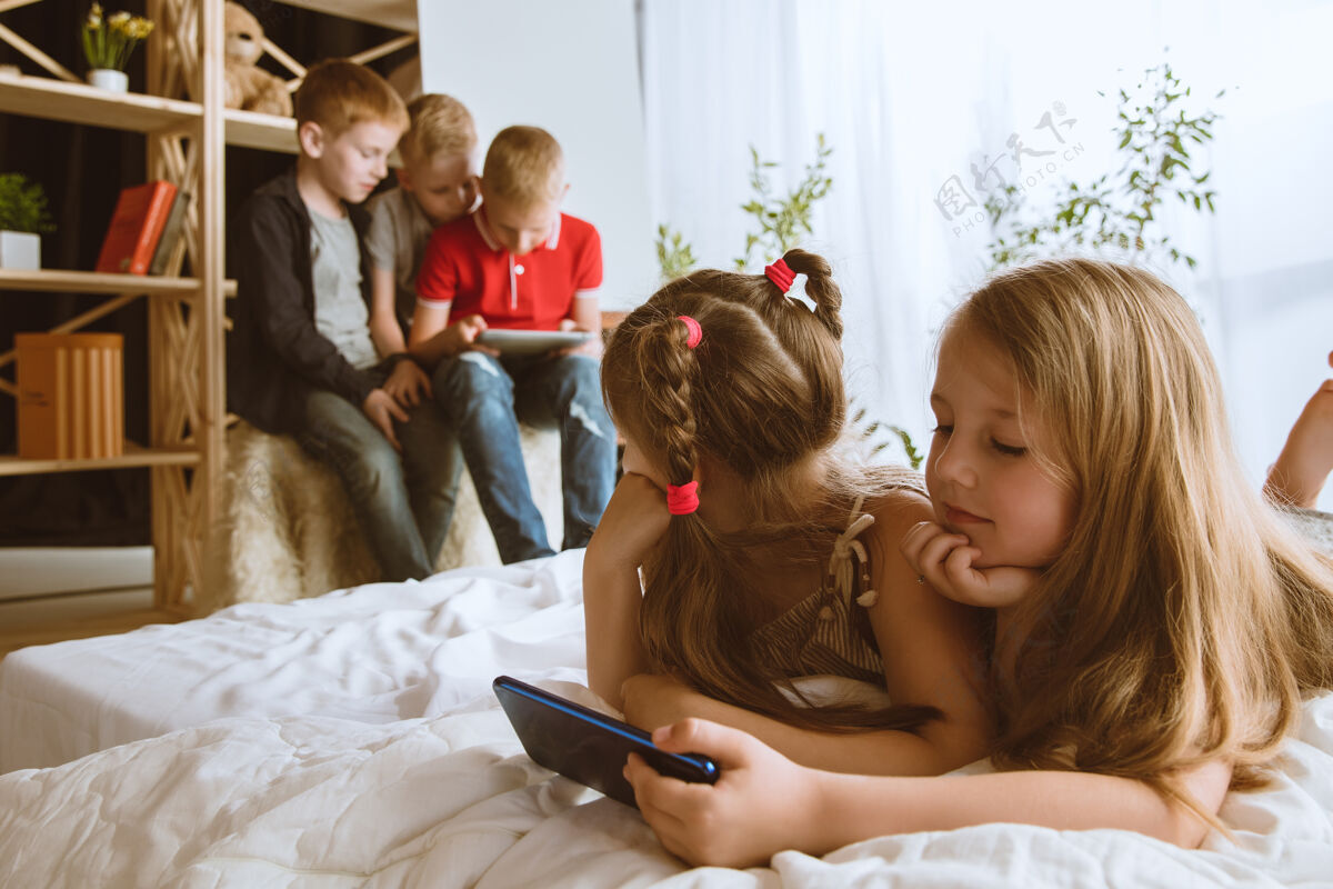 互联网男孩和女孩在家里使用不同的小玩意孩子们带着智能手表 智能手机和耳机自拍 聊天 游戏 看视频孩子们和现代科技的互动技术乐趣教育