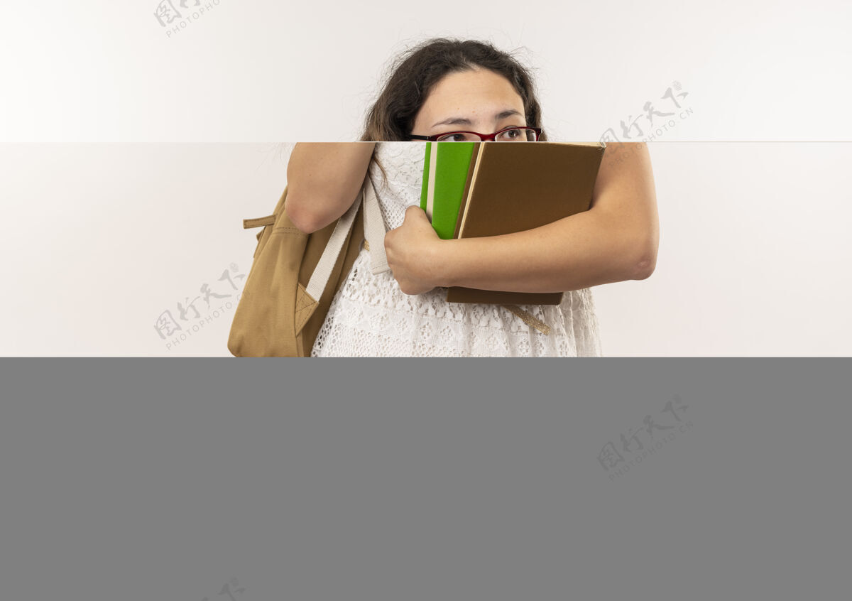 眼镜印象深刻的年轻漂亮的女学生戴着眼镜 背着书包 看着和指着白色隔离的一面年轻壁板指