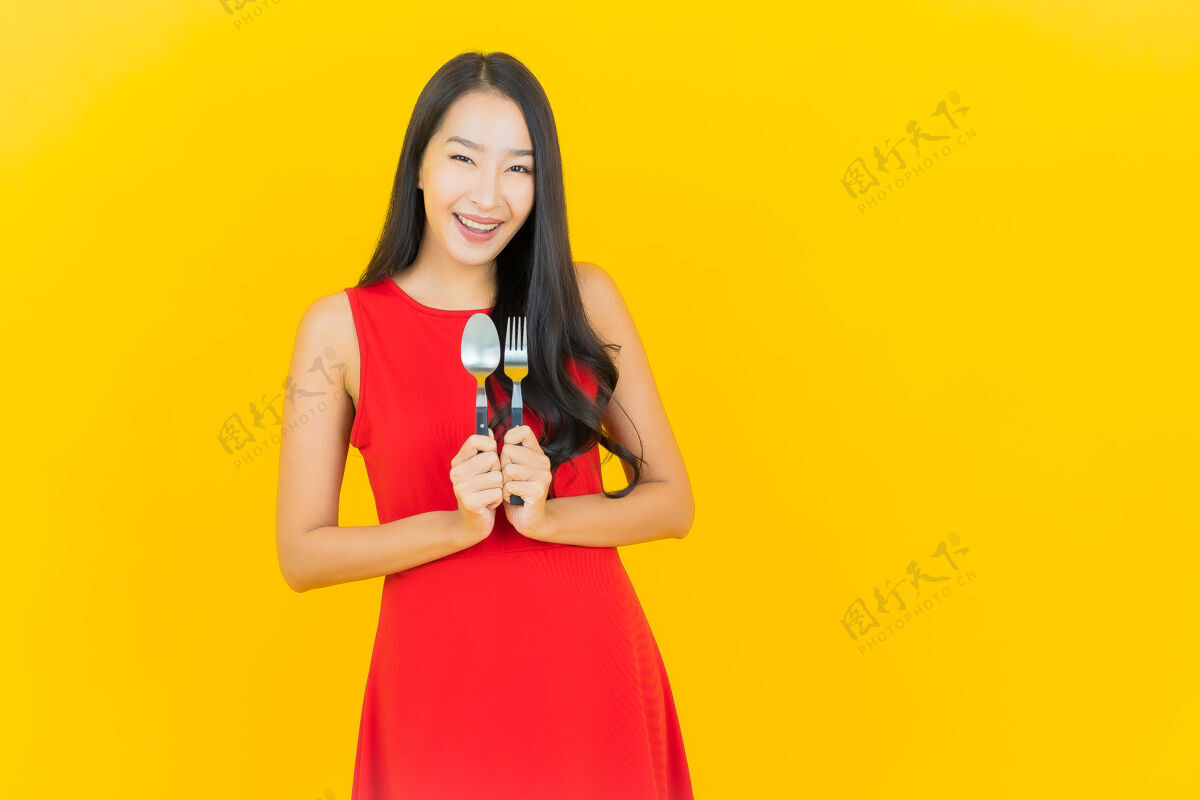 休闲画像美丽的亚洲年轻女子微笑着用勺子和叉子在黄色的墙上餐具勺子亚洲人