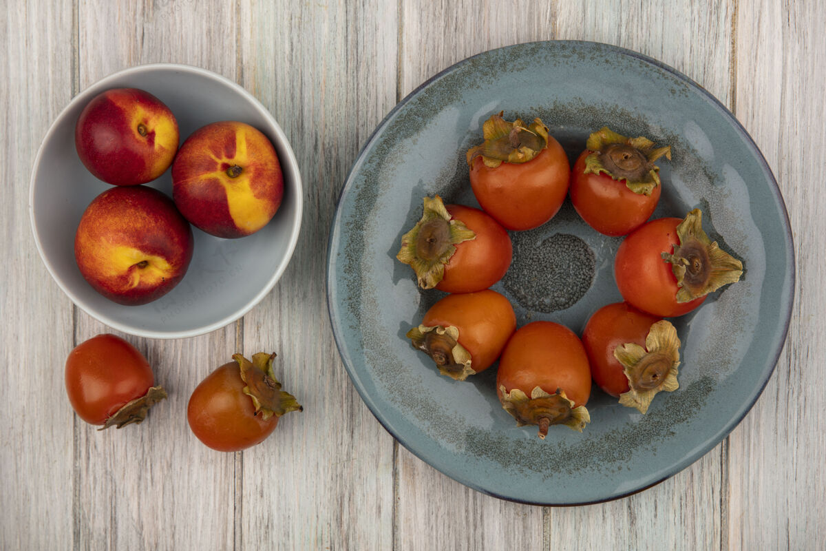 健康新鲜的桃子和软柿子放在一个盘子里的灰色木制背景上的顶视图水果灰色观