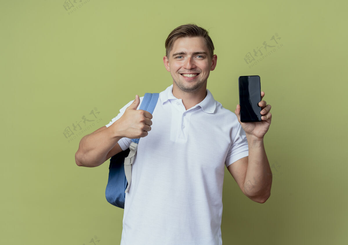 穿面带微笑的年轻帅气男学生背着书包拿着电话 他的大拇指孤立地竖在橄榄绿的背景上学生橄榄电话