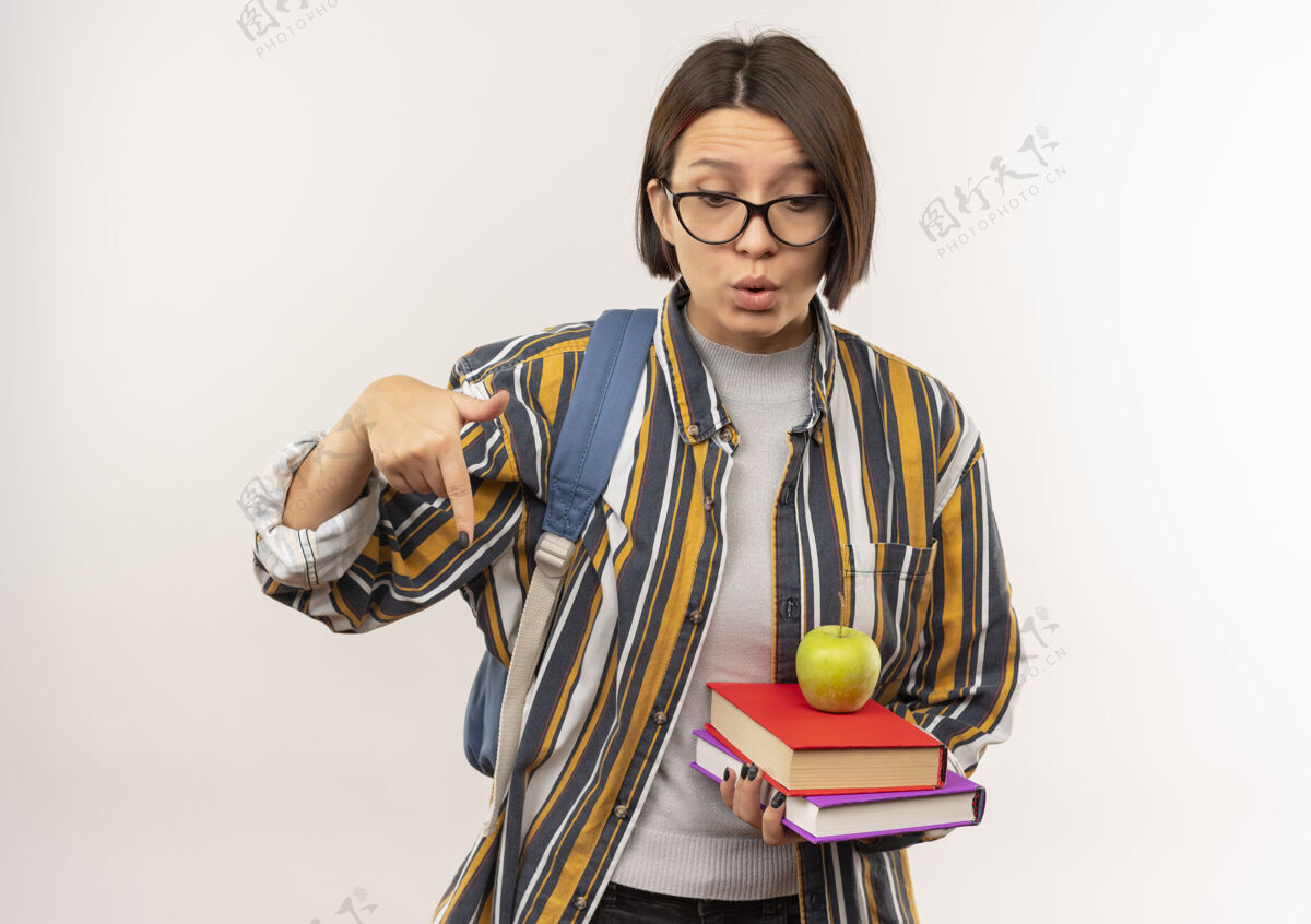 苹果给人印象深刻的年轻女学生戴着眼镜 背着包 手里拿着书 上面有苹果 指着白纸 孤零零地往下看学生指戴