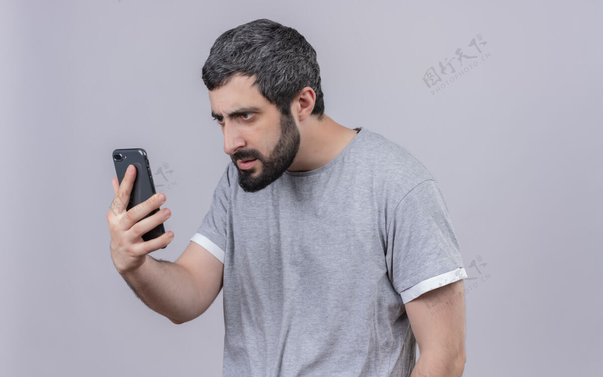 年轻一个年轻英俊的白人男子拿着手机 看着手机 手机被隔离在白色的背景上 还有复印空间帅气抱着手机