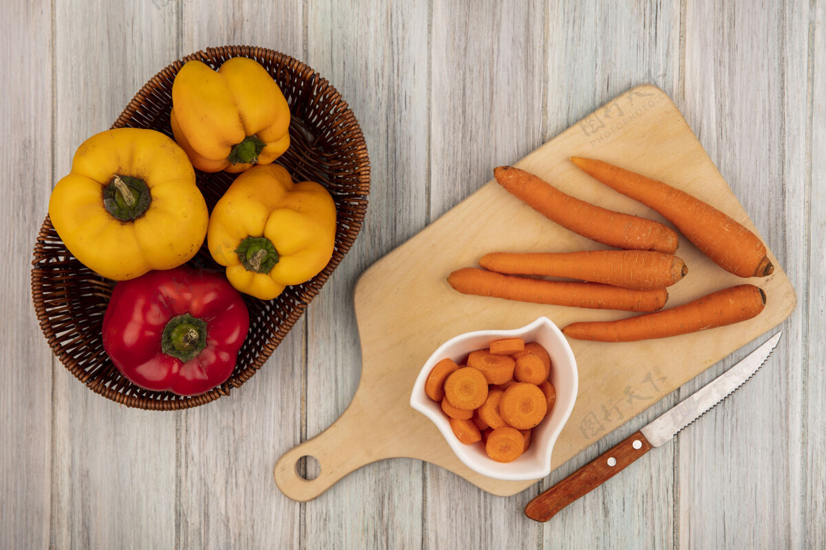 板顶视图新鲜五颜六色的甜椒与胡萝卜桶上的木制厨房板与刀在灰色的木制背景铃铛桶食物
