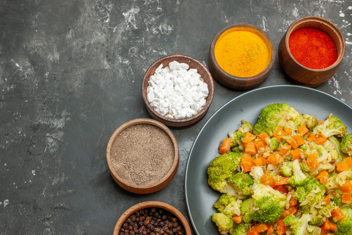 一餐半杯健康餐 黑盘子上放花椰菜和胡萝卜 灰色桌子上放香料胡椒粉米饭午餐