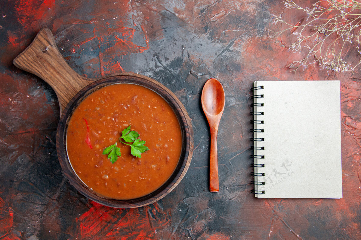 勺子番茄汤放在棕色的砧板上 笔记本放在五颜六色的桌子上餐厅碗容器