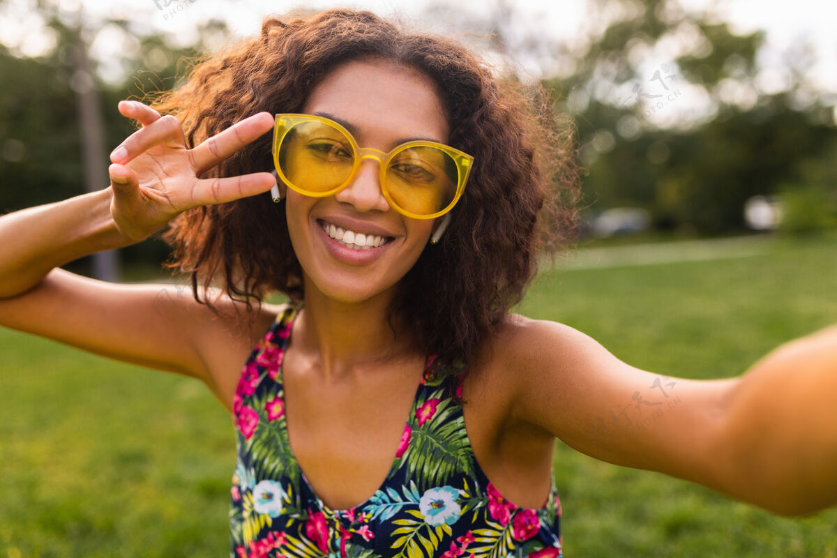 眼镜年轻时尚积极的黑人女性 自拍 戴着无线耳机听音乐 在公园里玩得很开心 夏日时尚 五颜六色的时髦装扮五颜六色享受酷