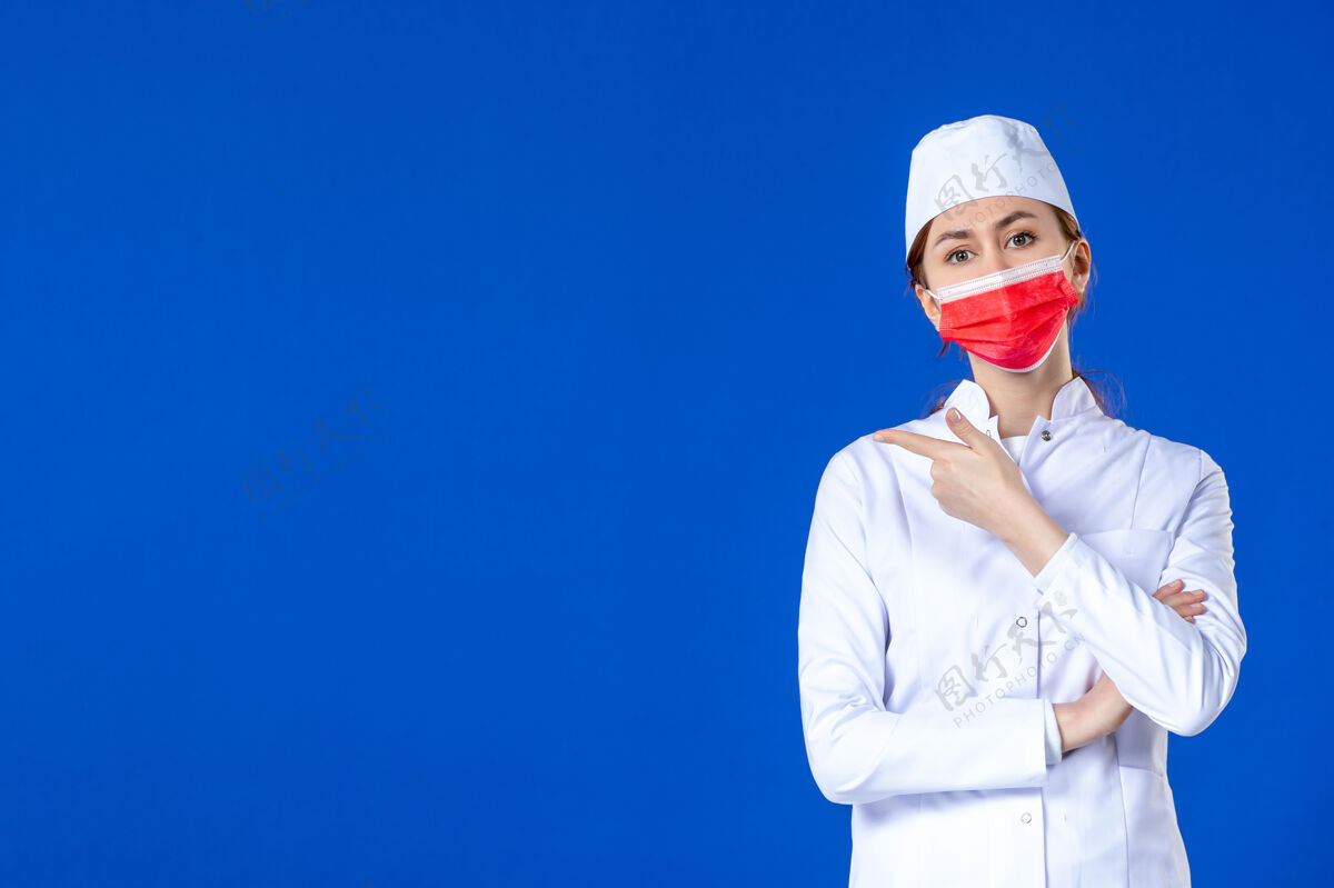 防护正面图身着医疗服的年轻护士 蓝色墙上戴着红色防护面具年轻护士药正面