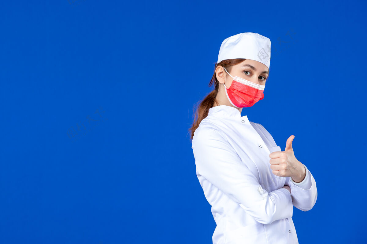 年轻护士正面图蓝色墙上戴着红色面罩的年轻护士 穿着医疗服前面面罩药