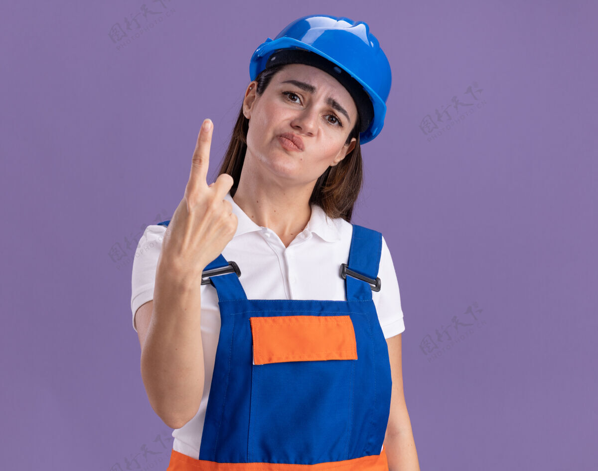 令人讨厌一个穿着制服的年轻建筑工人在紫色的墙上展示一个孤立的女人制服表演年轻