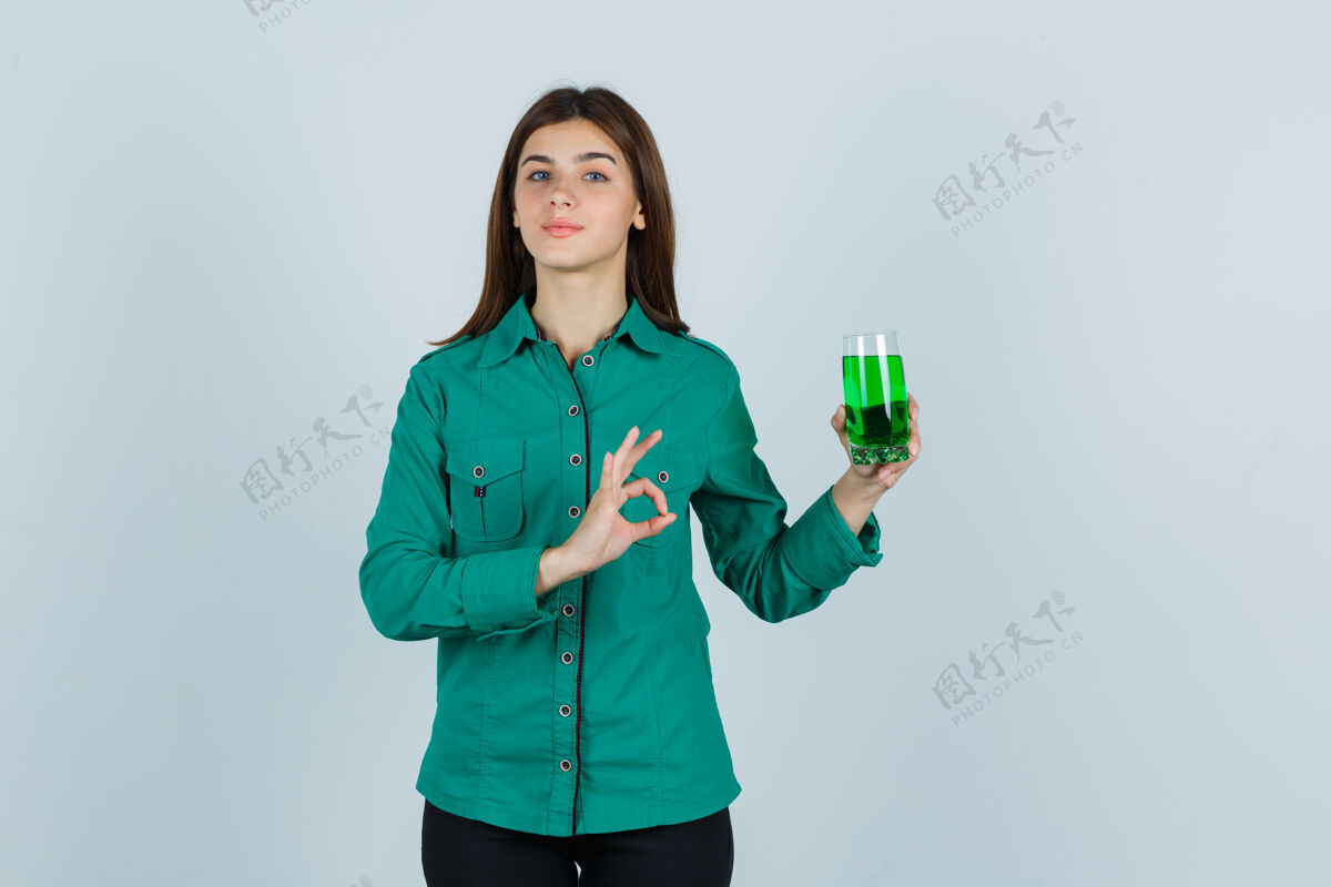 裤子年轻的女孩拿着一杯绿色液体 穿着绿色上衣 黑色裤子 看起来很高兴 正面照时尚自然人